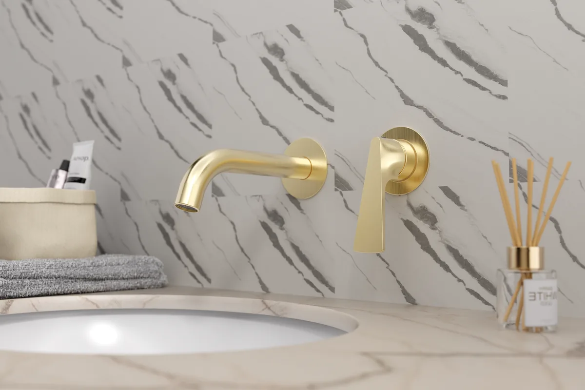 Brushed gold wall-mounted basin faucet with separate spout and handle on a marble bathroom wall